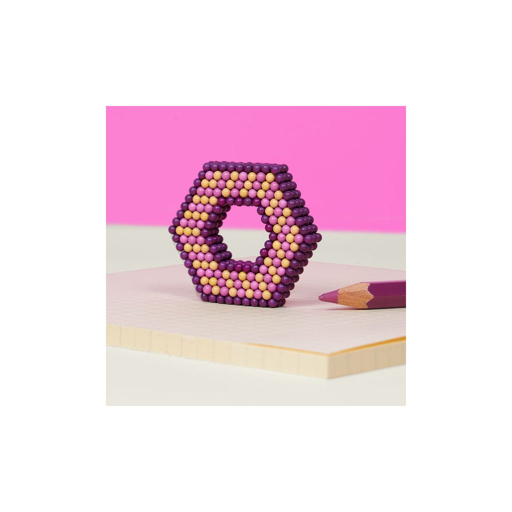 Speks magnetic fidget balls arranged in hexagonal shape with purple, pink and yellow spheres on pink background